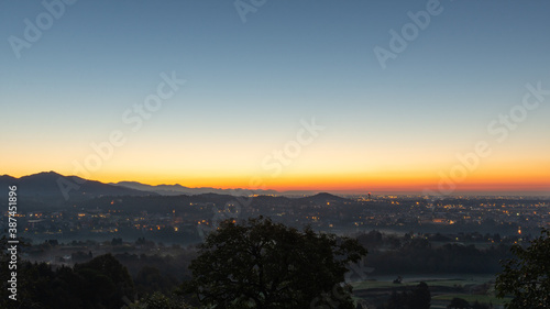 A clear sky lights up during the sunrise over the plain with the last city lights © Brambilla Simone