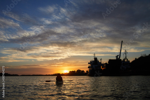 Sillouette of man kayaking on the Danube river at sunset near ship © watcherfox