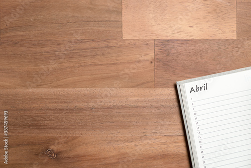 Blank page of a daily planner in Spanish for the month of April on a wooden desk