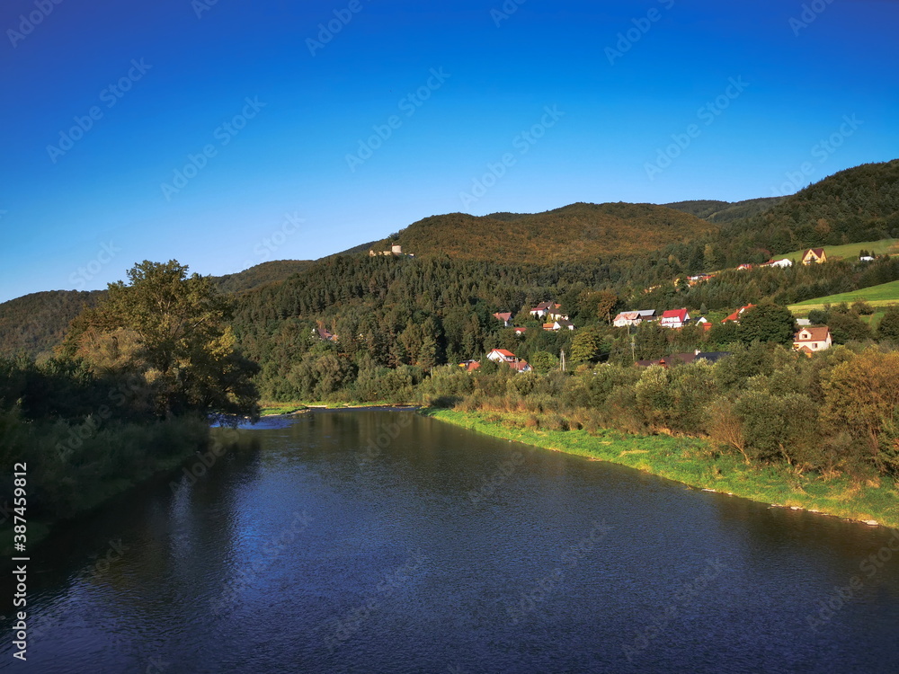 The river flows among the autumn Beskid Sadecki mountains. The Poprad river in the town of Rytro.