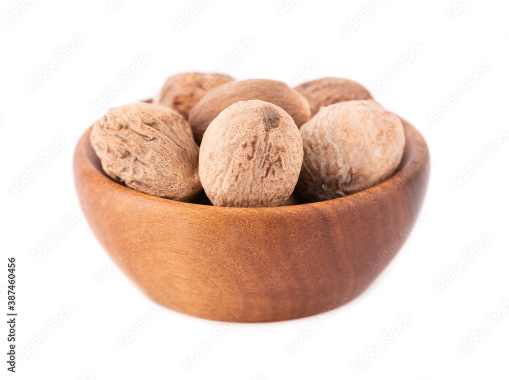 Nutmeg isolated on white background. Dry whole nutmeg in wooden bowl. Close-up.