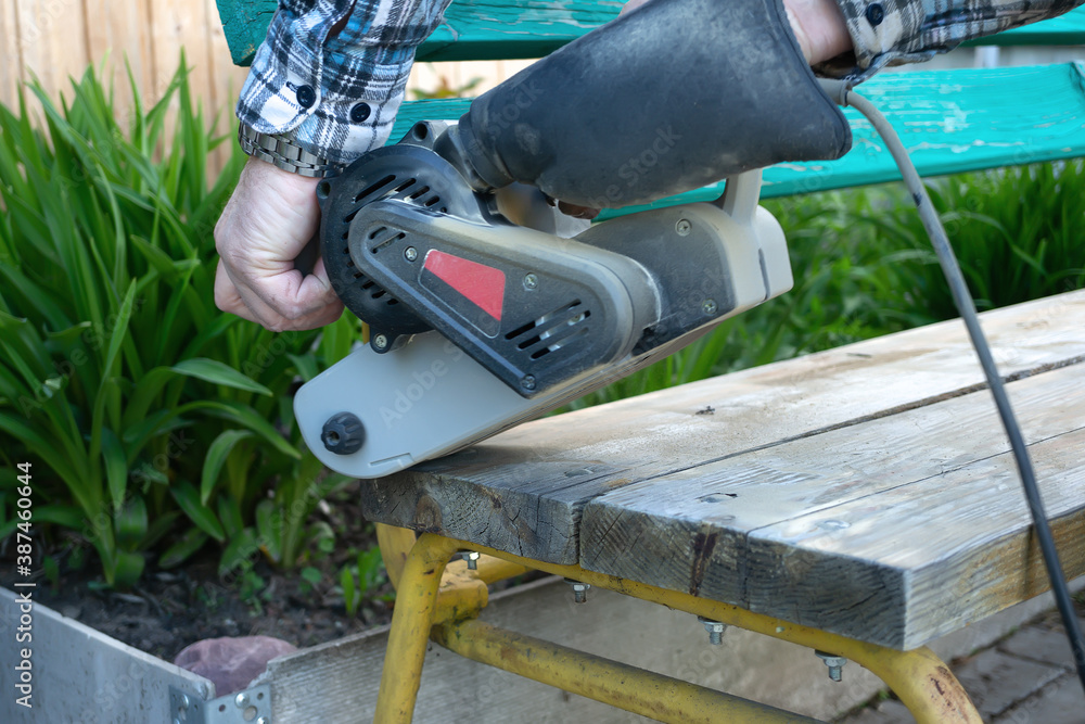 Landscaping of the garden. handyman sharpens a wooden bench on the street in the garden. master removes a layer of dry paint from the wood surface using an electric sander