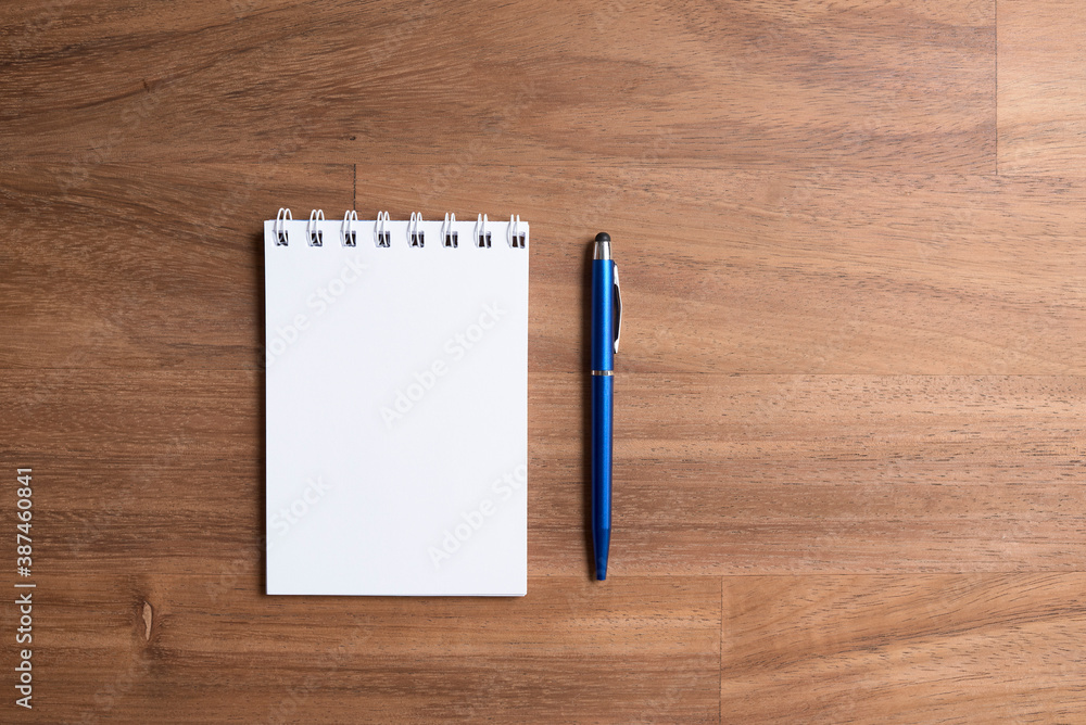 Spiral notebook, opened on a blank page, next to a blue pen, on a wooden desk Spiral notebook, opened on a blank page, next to a blue pen, on a wooden desk