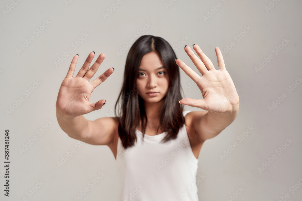 Portrait of young asian woman wearing white shirt having serious confident look while making stop gesture with two hands isolated over grey background Portrait of young asian woman wearing white shirt having serious confident look while making stop gesture with two hands isolated over grey background