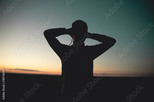 silhouette of a man at sunset. Hands behind the head.