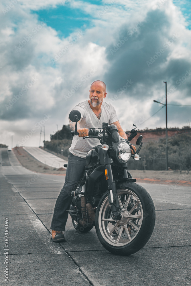 Fototapeta premium Motociclista hombre mexicano en carretera sobre su motocicleta con chaqueta de cuero y botas