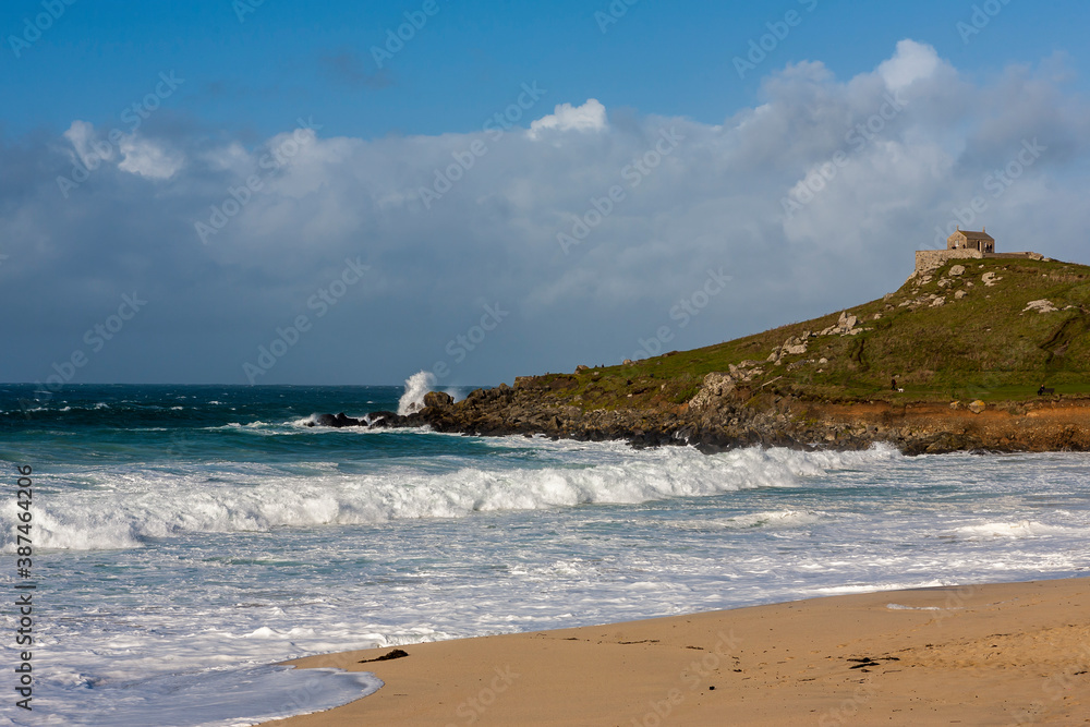 Rough seas on Porthmeor Beach, St. Ives, Cornwall, UK: St Nicholas Chapel on St Ives Head beyond