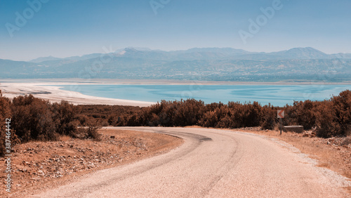 Scenic winding gravel road with a view of a lonely rocky mountain in the countryside area in Turkey. Burdur lake at the background