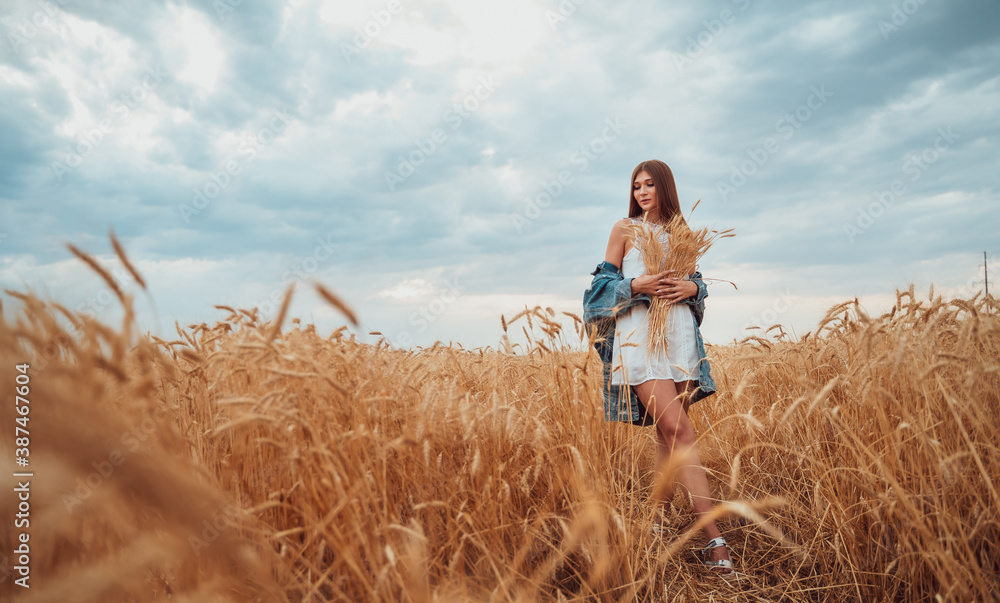 young woman in a white dress and denim jacket stands in the field. young woman in a white dress and denim jacket stands in the field.