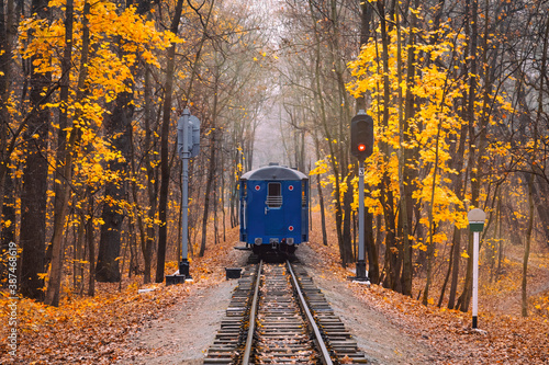 Old vintage blue railway train back view on the track rails goes away. Railroad single track through the woods in autumn. Fall landscape. red stop semaphore signal.