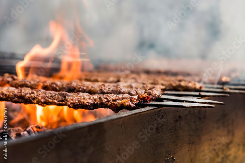 Traditional Adana kebab grilled on a grill with orange coloured flame and smokes, close up
