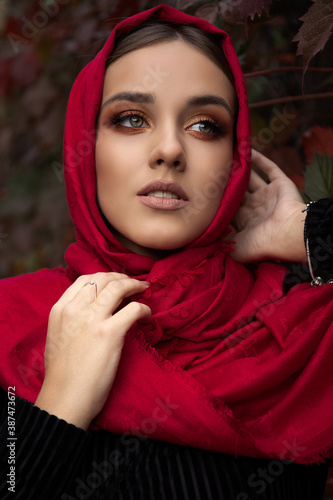 Close up portrait of beautiful young girl with incredible autumn makeup walks among the autumn colorful gardens in a beautiful kerchief in Marsala color. photo