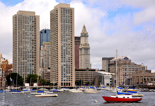 Scenic cityscape of Boston skyline and waterfront with tall modern buildings, sailboats anchored in harbor, and the Custom House Tower (designated a Boston Landmark). photo