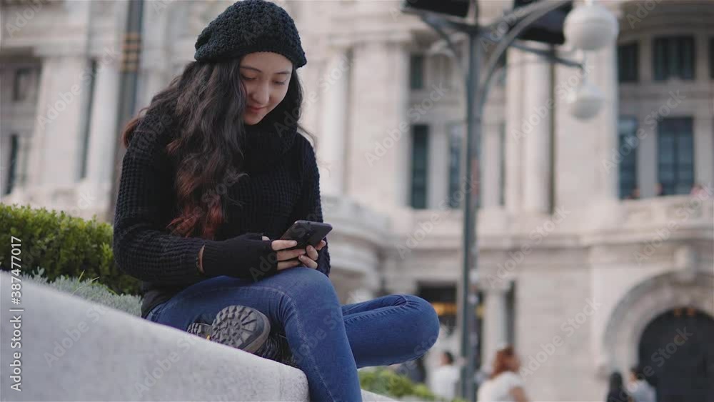 Vista de una adolescente en las calles de la Ciudad de México con ropa de abrigo en una tarde de otoño, una niña con su teléfono celular jugando o enviando un mensaje