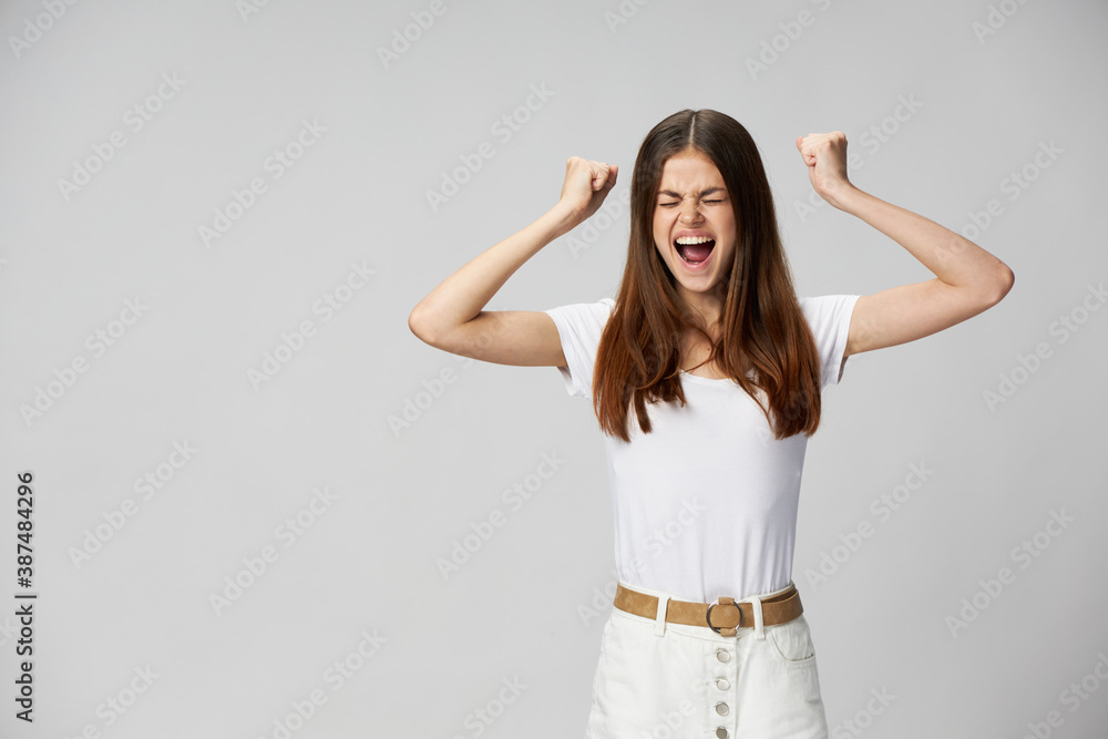 Energetic woman with closed eyes shouts with clenched hands into a fist on a light background 