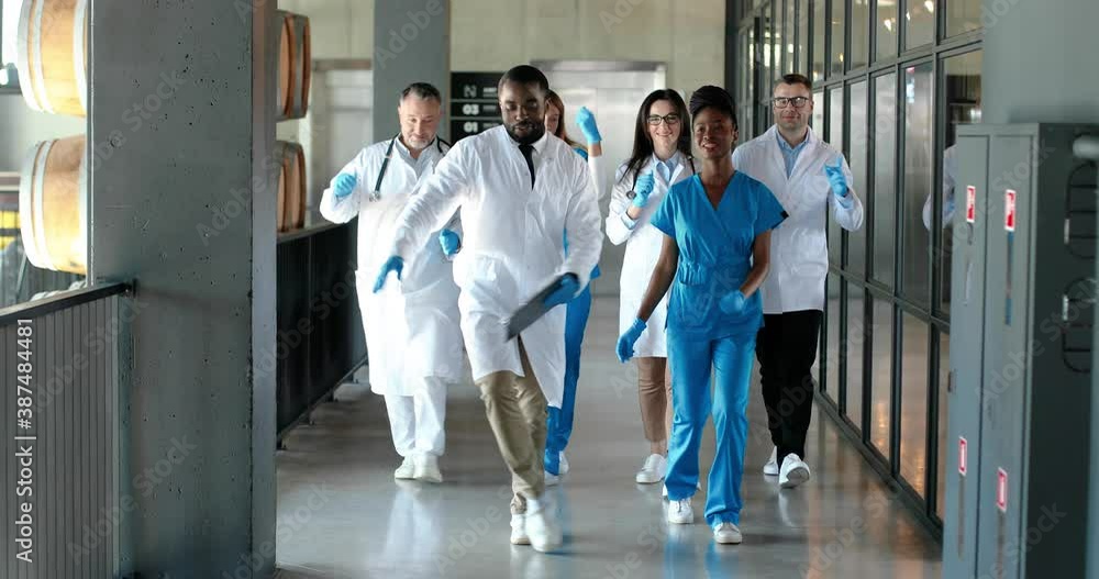 Mixed-races team of males and females doctors and nurses walking and dancing funny at corridor of hospital. Multi ethnic medics in medical uniforms dance and doing fun moves in clinic. Docs having fun Mixed-races team of males and females doctors and nurses walking and dancing funny at corridor of hospital. Multi ethnic medics in medical uniforms dance and doing fun moves in clinic. Docs having fun