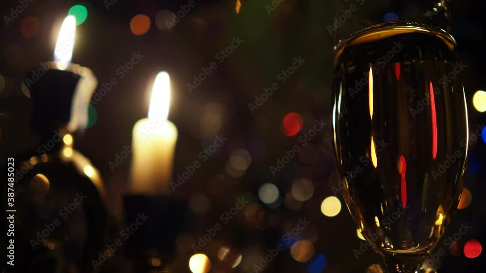 Christmas, New year, Holidays. Bubbles in a champagne glass against a background of candles and flickering colored lights. Background video. Close up. Christmas, New year, Holidays. Bubbles in a champagne glass against a background of candles and flickering colored lights. Background video. Close up.