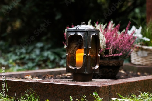 Obraz na plátně Grave lantern made of metal with burning candle in front of grave decoration in