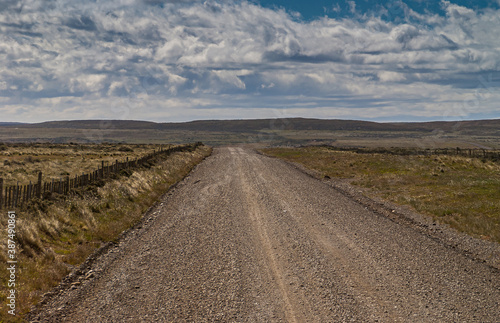 Punta Arenas  Chile - December 12  2008  Brown pebbles and dirt road to Riesco Island in endless dry landscape under spectacular blue-white cloudscape.