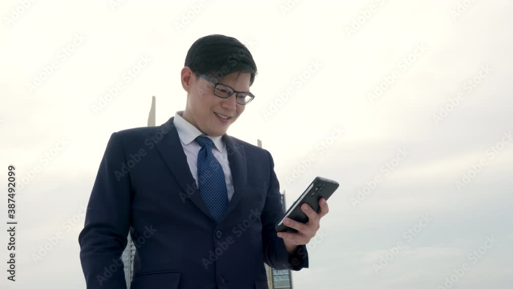 4K Happy Asian businessman office worker using smartphone with internet working outdoor at office building rooftop. Successful business man entrepreneur working with wireless technology in the city 4K Happy Asian businessman office worker using smartphone with internet working outdoor at office building rooftop. Successful business man entrepreneur working with wireless technology in the city
