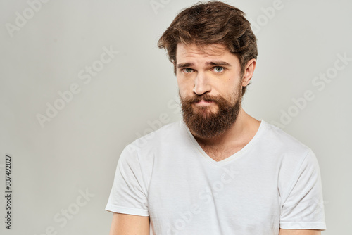 A man in a white t-shirt with a beard emotions displeased facial expression light background