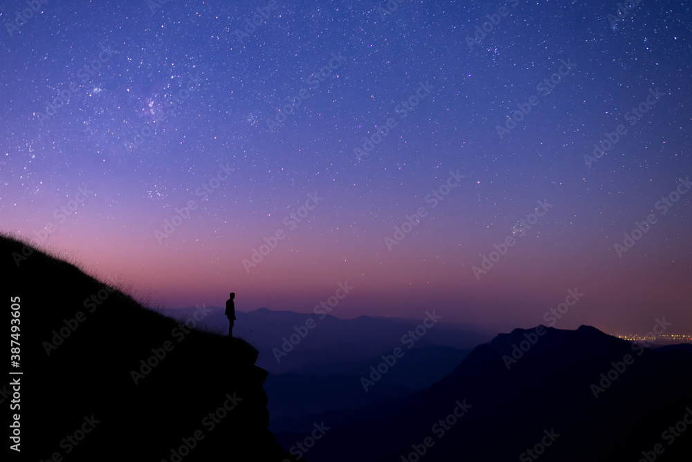 Silhouette of young tourists standing and watching the view of star and milky way and sunrise alone on the top of the mountain before sunrise. He is happy to be with herself and nature.
