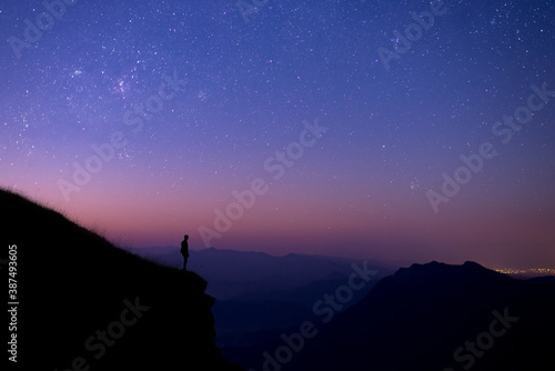 Silhouette of young tourists standing and watching the view of star and milky way and sunrise alone on the top of the mountain before sunrise. He is happy to be with herself and nature.