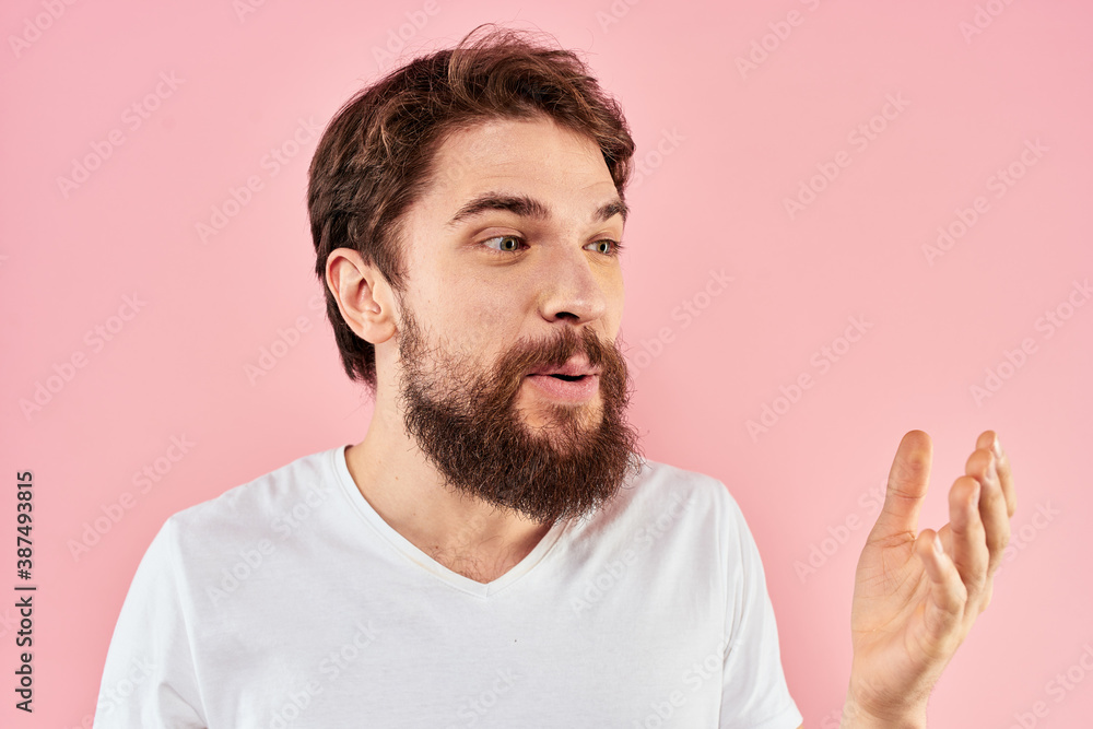 Bearded man in white t-shirt gesturing with hands facial expression close up pink background Bearded man in white t-shirt gesturing with hands facial expression close up pink background