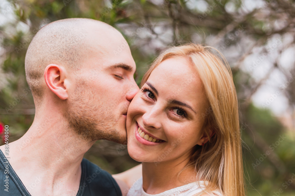 Man kisses her lover. Young couple kisses on the cheek. Caucasian couple outdoors. Man kisses her lover. Young couple kisses on the cheek. Caucasian couple outdoors.