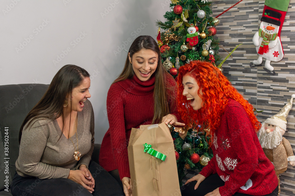 Fototapeta premium Three happy friends opening a gift very surprised at Christmas 