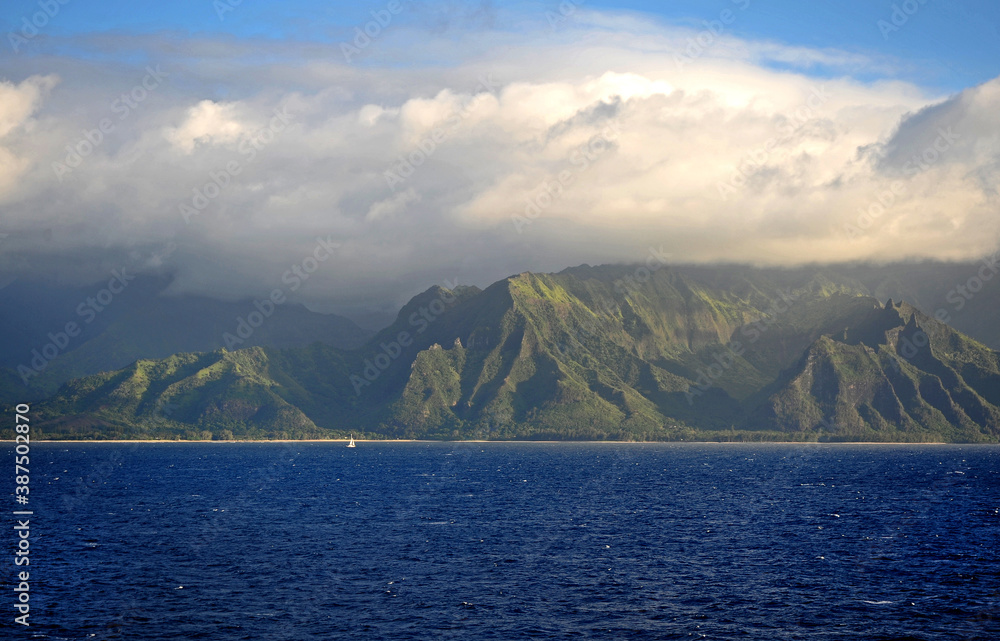 The Napali rugged coastline Hawaii, a small yacht is dwarfed by the dynamic rocky coast.