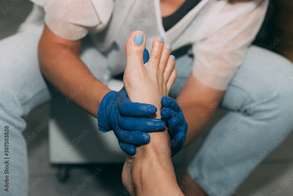 Fototapeta premium Close-up of Pedicure in salon. Foot care treatment and nail. Foot massage during the pedicure process. Master in blue gloves makes pedicure with manicure machine. Concept of beauty care and health