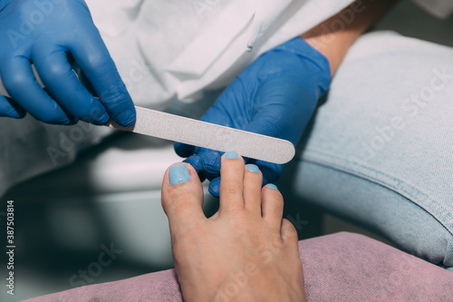 Pedicure in salon. Foot care treatment and nail. File filing with a nail file after applying gel polish. Master in blue gloves makes pedicure with manicure machine. Concept of beauty care and health