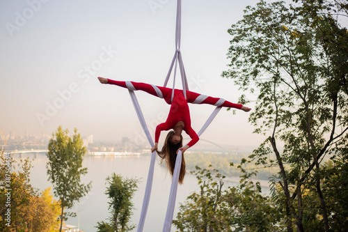 silhouette of a beautiful and professional Aerial silk artist practicing in the red suit under the famous glass bridge over the Kiev city on a sunset  © Kucheryaha