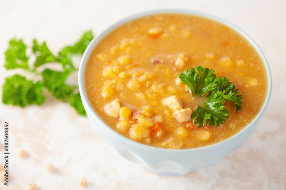 Pea soup with pieces of bacon and parsley in blue bowl on a white background.