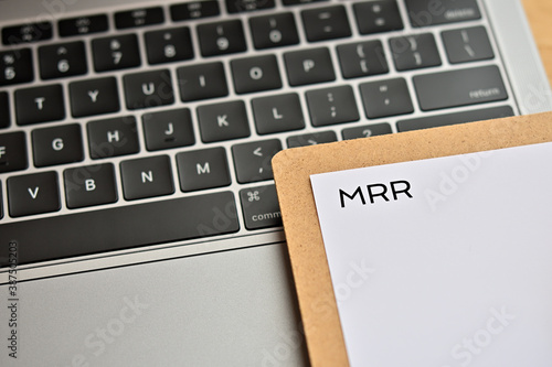 A piece of paper with the word "MRR" written on it sits on the keyboard. That's an acronym for "Monthly Recurring Revenue". Close up. 