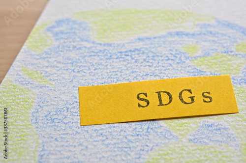 There is a sticky note with the word "SDGs" written on top of a sketchbook with an illustration of the earth. It is an acronym that stands for Sustainable Develoment Goals.