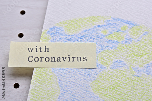 There is a sketchbook with an illustration of the earth and a sticky note with the words "with Coronavirus" on it.