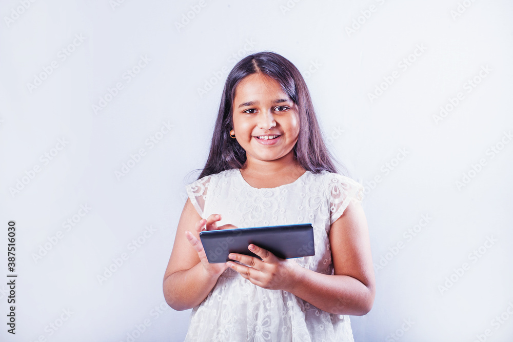 Cute Indian little girl using tablet computer on her studio portrait on white background Cute Indian little girl using tablet computer on her studio portrait on white background