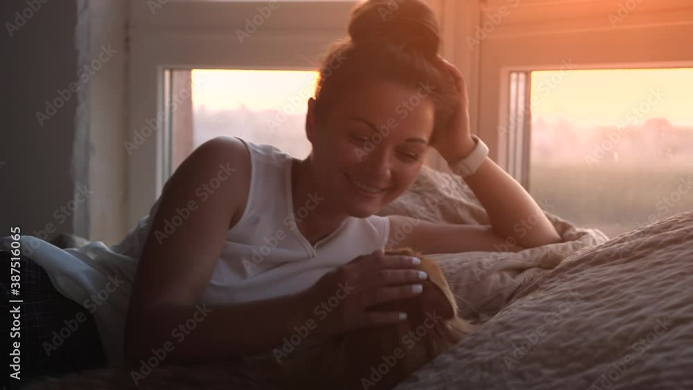 Young pretty woman lying on the bed with Maine Coon cat by the window during sunset time Young pretty woman lying on the bed with Maine Coon cat by the window during sunset time