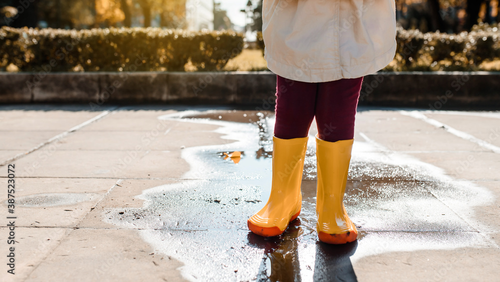 child legs in yellow boots standing in the middle of a puddle after rain.