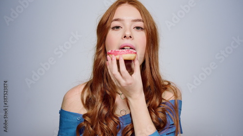 Smiling woman eating doughnut indoors. Excited girl having snack in studio