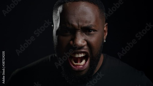 Wicked afro guy screaming on black background. Closeup man yelling in studio photo