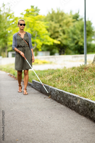 Blind woman walking on city streets, using her white cane to navigate the urban space better and to get to her destination safely photo