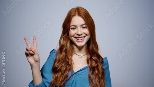 Wallpaper Mural Friendly redhead woman doing peace sign indoors. Joyful girl posing in studio Torontodigital.ca