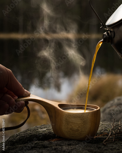 Freshly brewed coffee poured into a wooden cup at a campsite near a lake in the forests