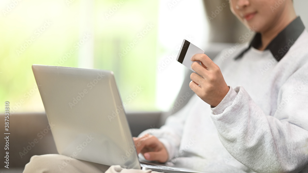 Cropped shot of a young woman holding credit card and using computer tablet on sofa at home. Cropped shot of a young woman holding credit card and using computer tablet on sofa at home.