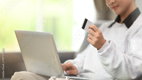 Cropped shot of a young woman holding credit card and using computer tablet on sofa at home.