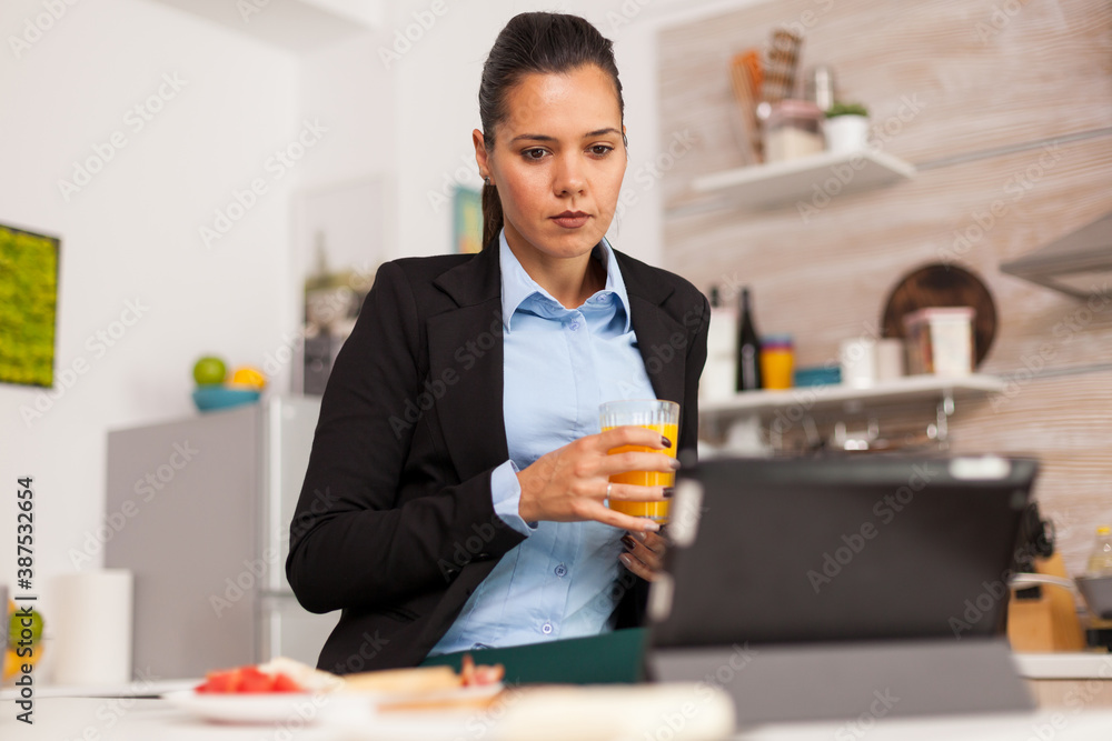 Business woman satisfied to the online project. Business woman reading the project online before going to work, using modern technology in the kitchen while eating a healthy meal