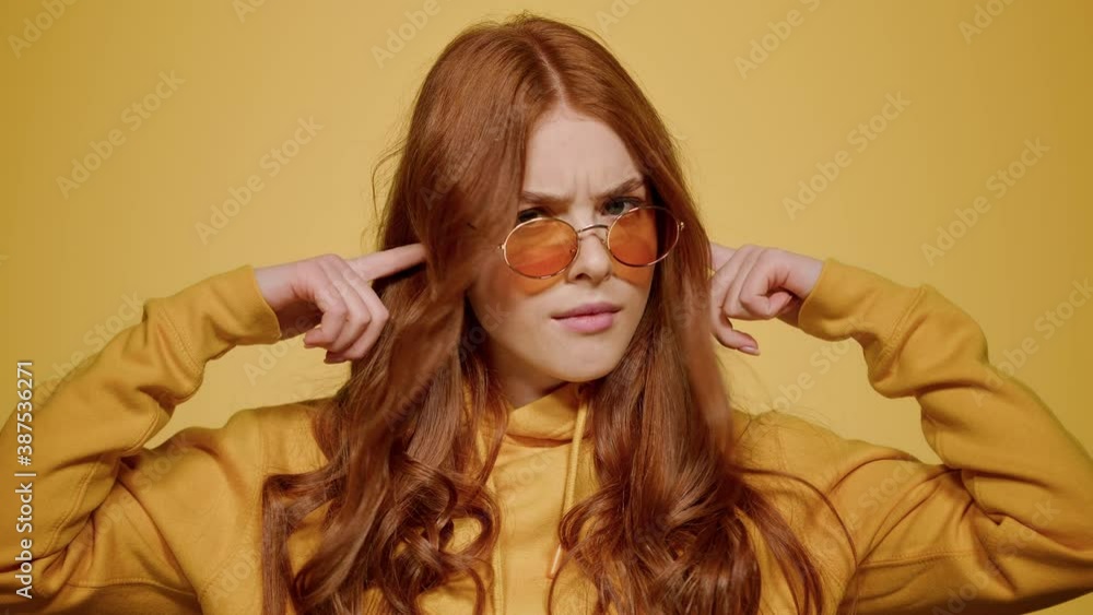 Agitated girl posing in studio. Woman closing ears on orange background Agitated girl posing in studio. Woman closing ears on orange background